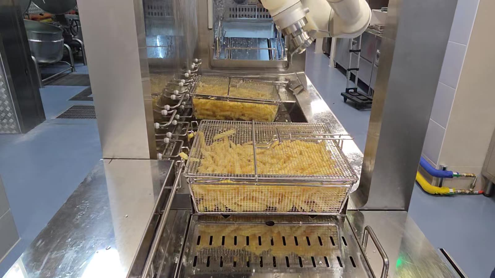 The robot cooking over a row of fry baskets in a working kitchen